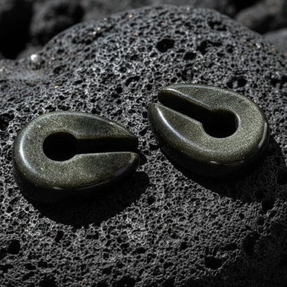 A pair of Golden Obsidian Stone Hangers (6-10mm) on volcanic rock with dramatic lighting.