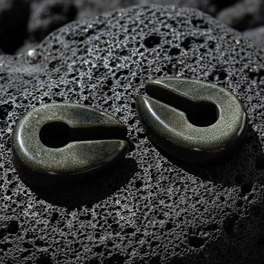A pair of Golden Obsidian Stone Hangers (6-10mm) on volcanic rock with dramatic lighting.