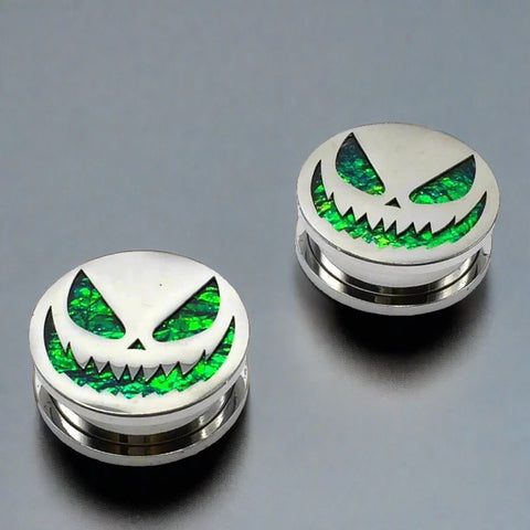Steel plugs featuring a menacing jack-o'-lantern face on a shimmering green opal background.