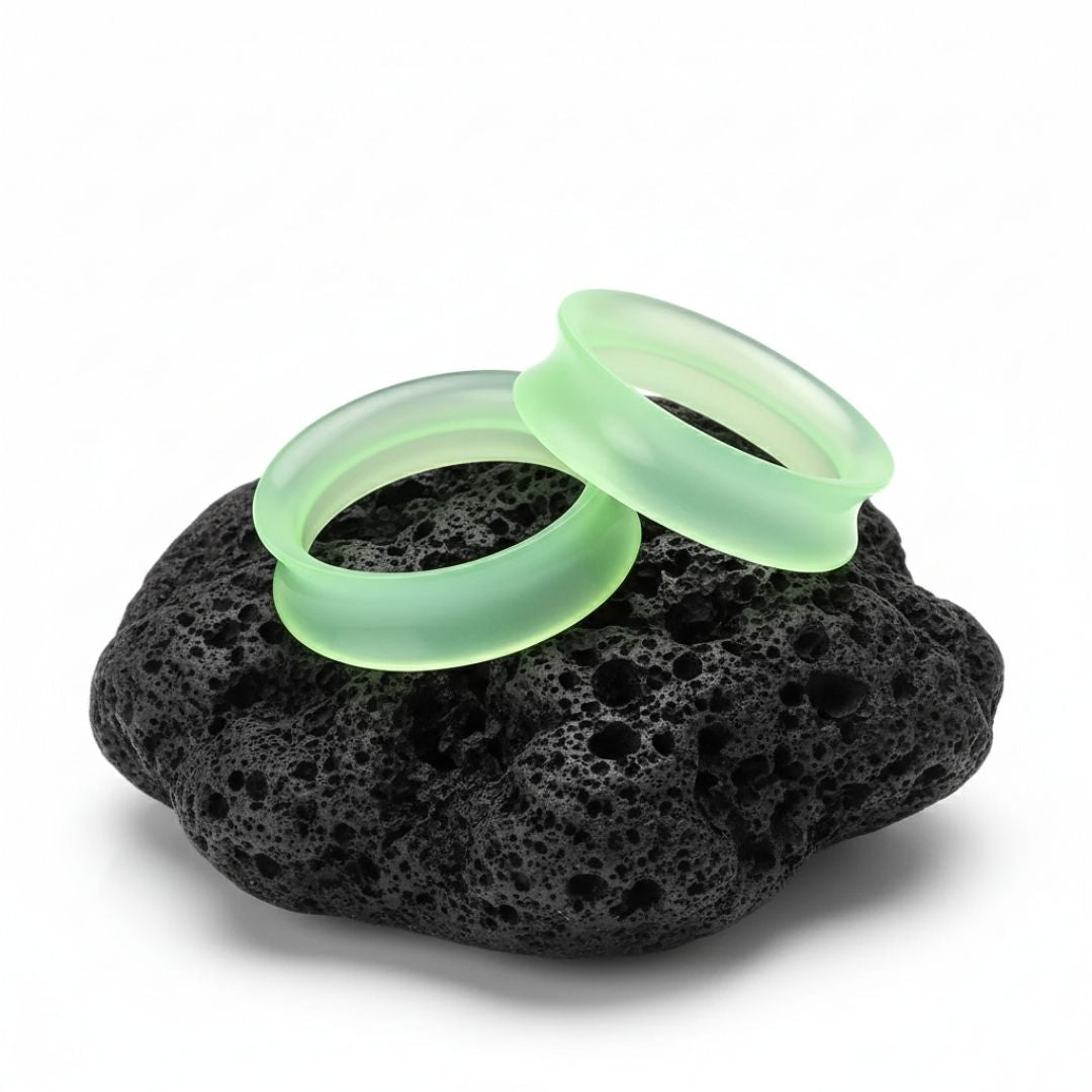 Pair of bright green silicone ear skins/tunnels displayed on a dark background. Flexible gauges for stretched piercing comfort.