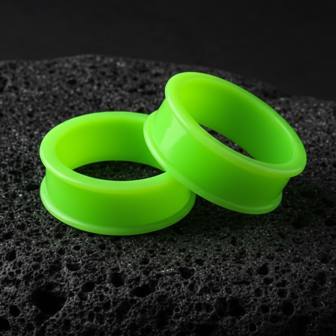 Close-up shot of neon green silicone tunnels (flexible eyelets) ranging in size, used for body modification.