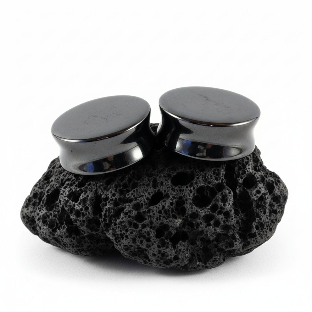 Pair of shiny dark grey Hematite stone plugs and gauges displayed on a black background, sizes 6mm to 25mm.