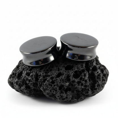 Pair of shiny dark grey Hematite stone plugs and gauges displayed on a black background, sizes 6mm to 25mm.