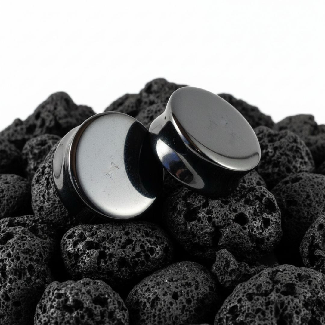 Pair of shiny dark grey Hematite stone plugs and gauges displayed on a black background, sizes 6mm to 25mm.