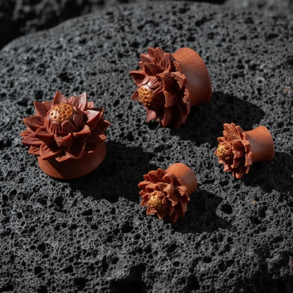 A pair of Carved Sawo Wood Lotus Plugs on dark volcanic rock with dramatic lighting.