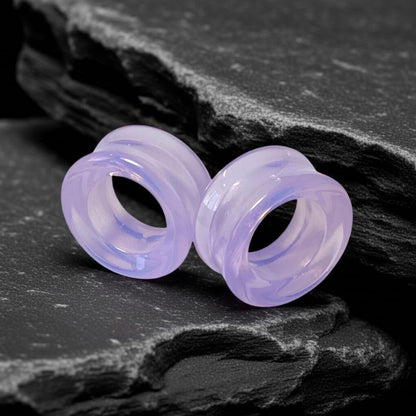 Pair of light purple ear gauges on a dark stone surface