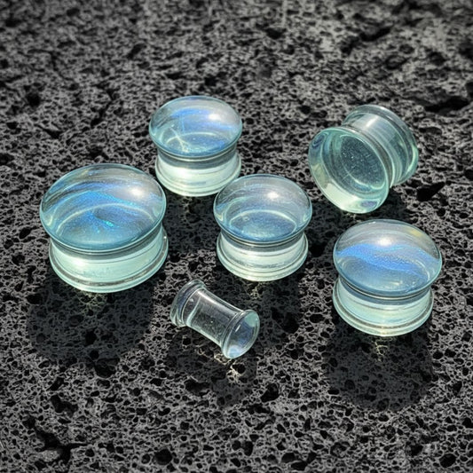 Ocean Current Glass Plugs (6mm-25mm) on dark volcanic rock with moody side lighting.