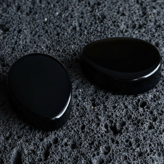 A pair of Onyx Stone Teardrop Plugs on volcanic rock with dramatic side lighting.