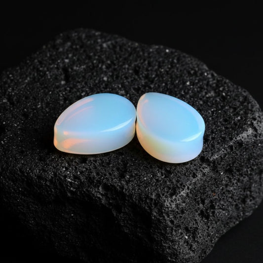 A pair of double flared Opalite teardrop plugs (gauges) displayed against a dark background for stretched ear jewelry alt fashion.