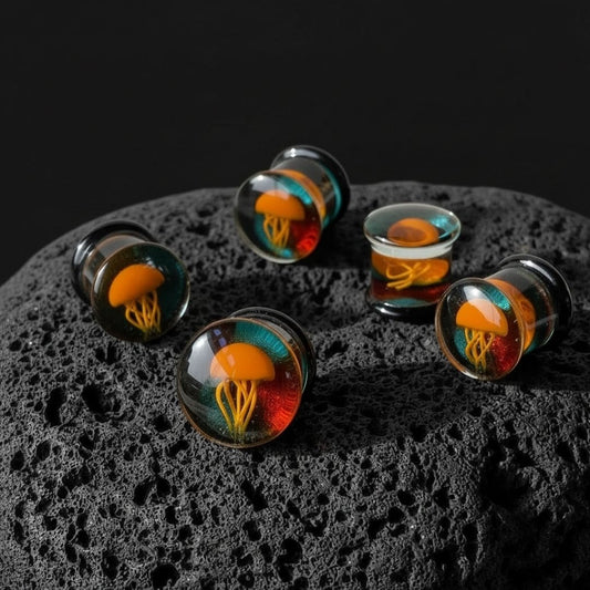 Orange Glass Jellyfish plugs (8mm-19mm) on dark volcanic rock with dramatic lighting.