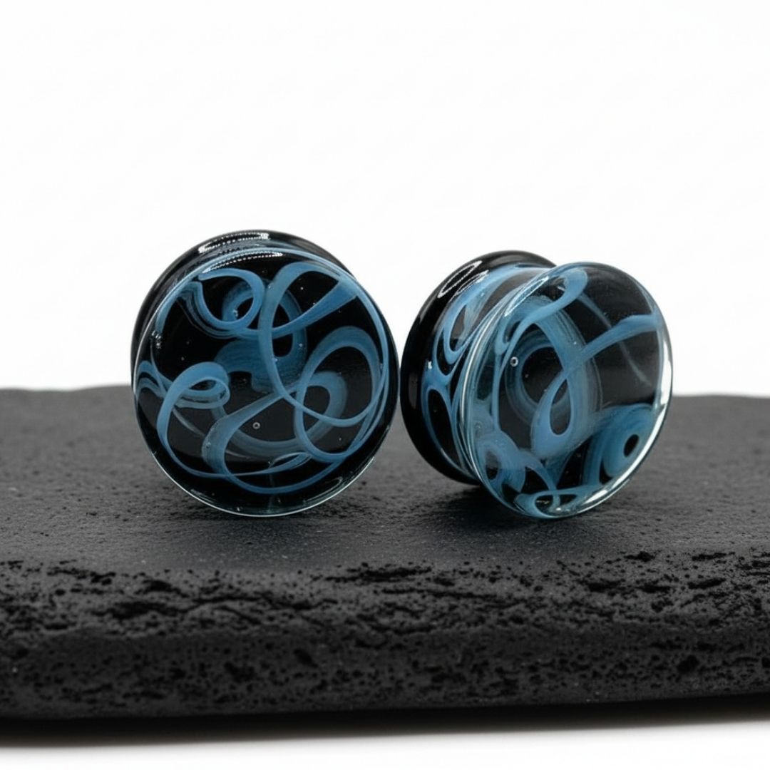 Pair of translucent glass plugs with dark smoky swirl patterns for stretched ear piercings, available in 6mm to 25mm.