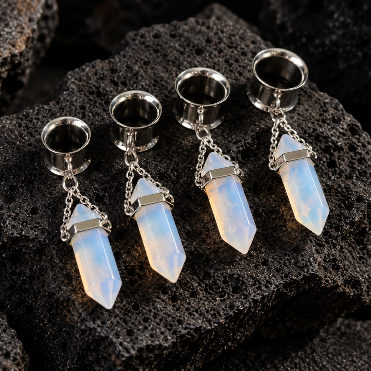 Steel Opalite Dangle Tunnels (6mm-16mm) resting on dark volcanic rock with sharp shadows.