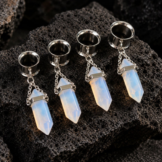 Steel Opalite Dangle Tunnels (6mm-16mm) resting on dark volcanic rock with sharp shadows.