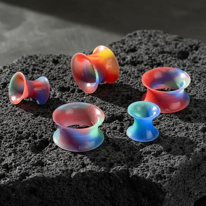 A pair of Rainbow Silicone Skins tunnels for 5mm-22mm gauges on dark volcanic rock.