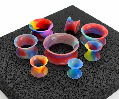 Rainbow Silicone Skins tunnels (5mm-22mm) on volcanic stone with a clean white background.