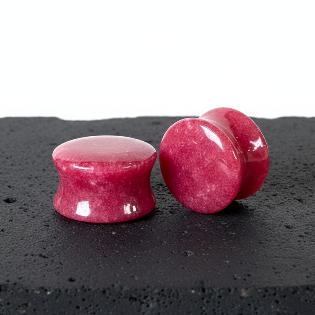 Close-up of a pair of polished, deep red jade stone ear plugs with a slight flare, showcasing their natural texture and color.
