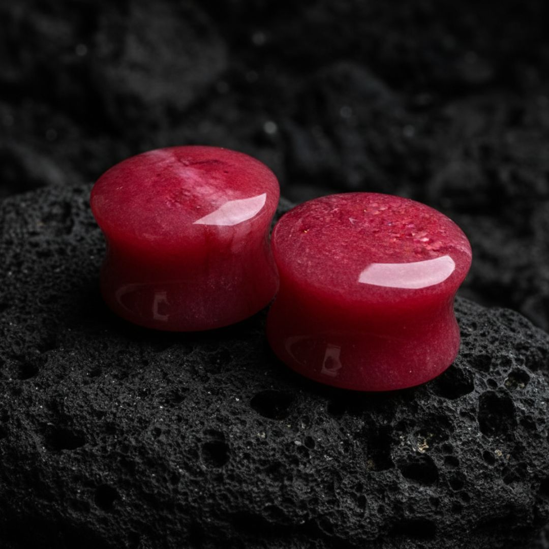 Two red stone plugs on a dark, textured surface