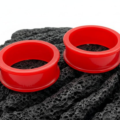 Pair of bright blood red silicone tunnels (flexible gauges) on a flat surface, showing the comfort fit material for large stretched ears.