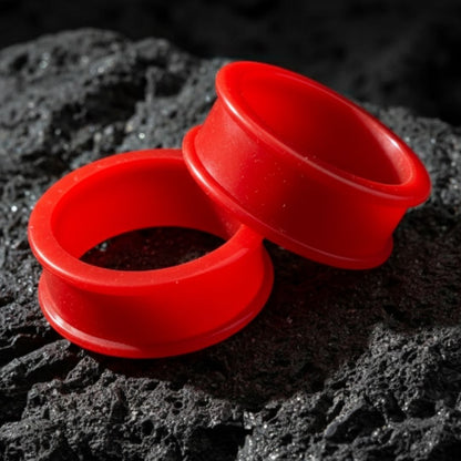 Pair of bright blood red silicone tunnels (flexible gauges) on a flat surface, showing the comfort fit material for large stretched ears.