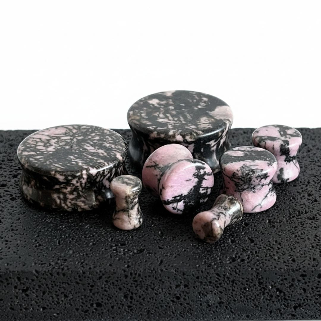 A pair of Rhodonite Stone Plugs, sizes 6mm-25mm, on stone against a white background.