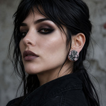 Close-up of a woman wearing rhodonite plugs in her stretched ear lobes with a dark background