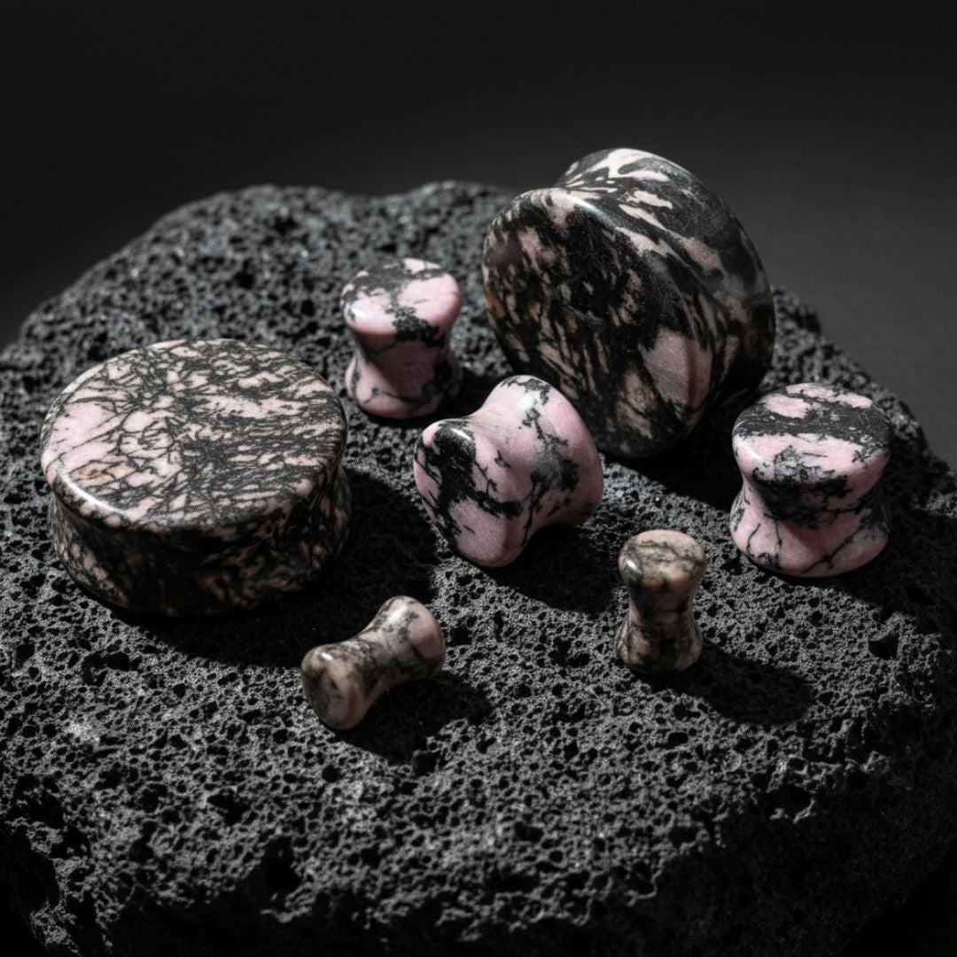 Rhodonite Stone Plugs (6mm-25mm) on dark volcanic rock with dramatic side lighting.