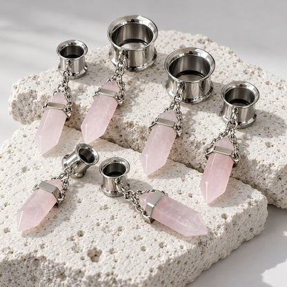 A pair of Steel Rose Quartz Dangle Tunnels on rock against a clean white background.