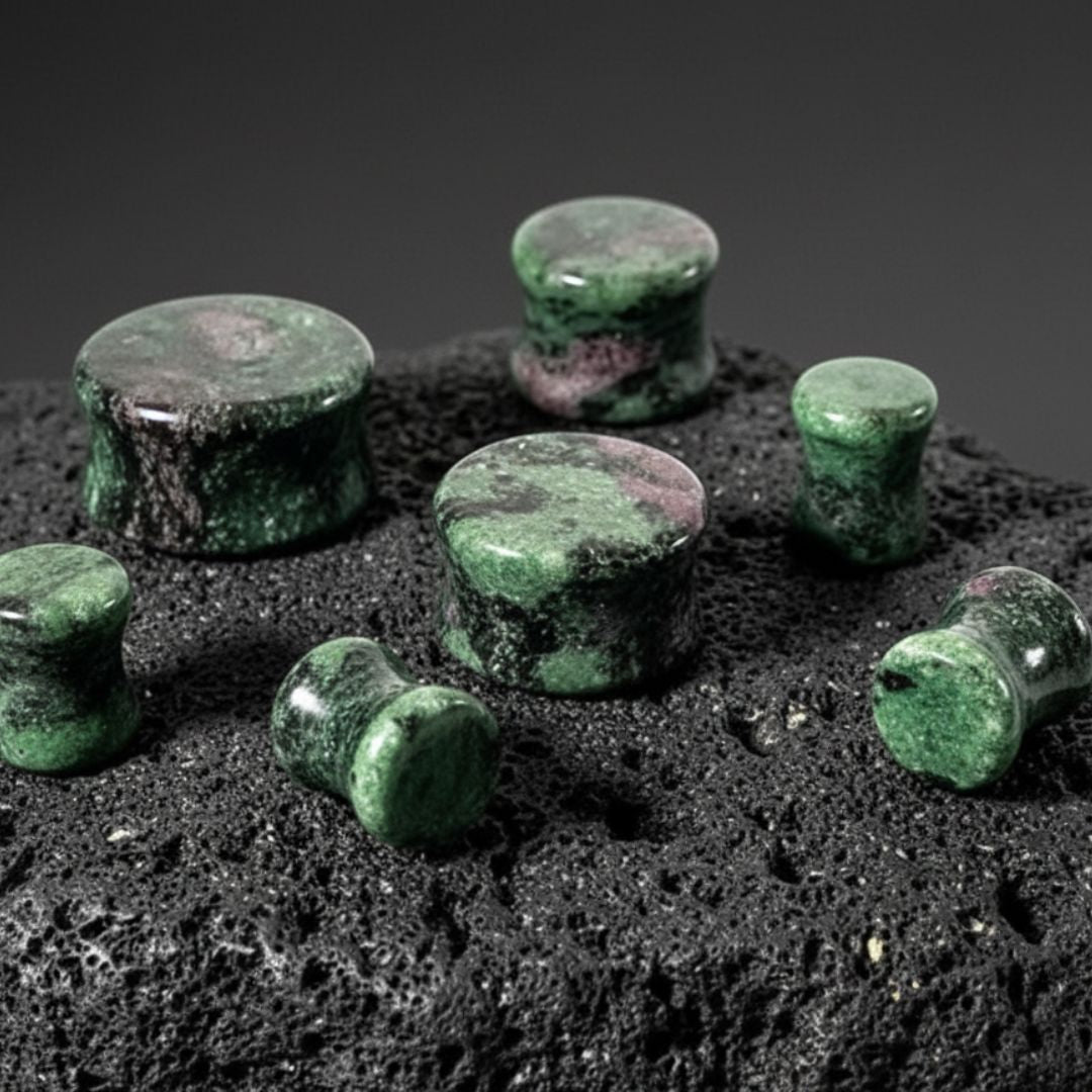 Ruby Zoisite Stone Plugs (6mm-25mm) on dark volcanic rock with dramatic side lighting.