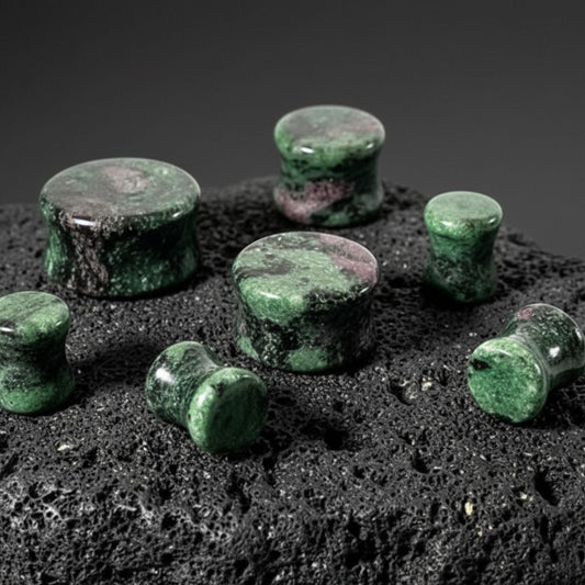 Ruby Zoisite Stone Plugs (6mm-25mm) on dark volcanic rock with dramatic side lighting.