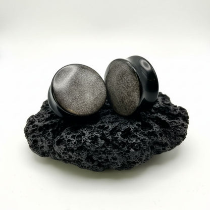 Pair of deep black Silver Obsidian stone plugs, polished, reflecting a subtle silver flash. Gauges displayed on a dark background.