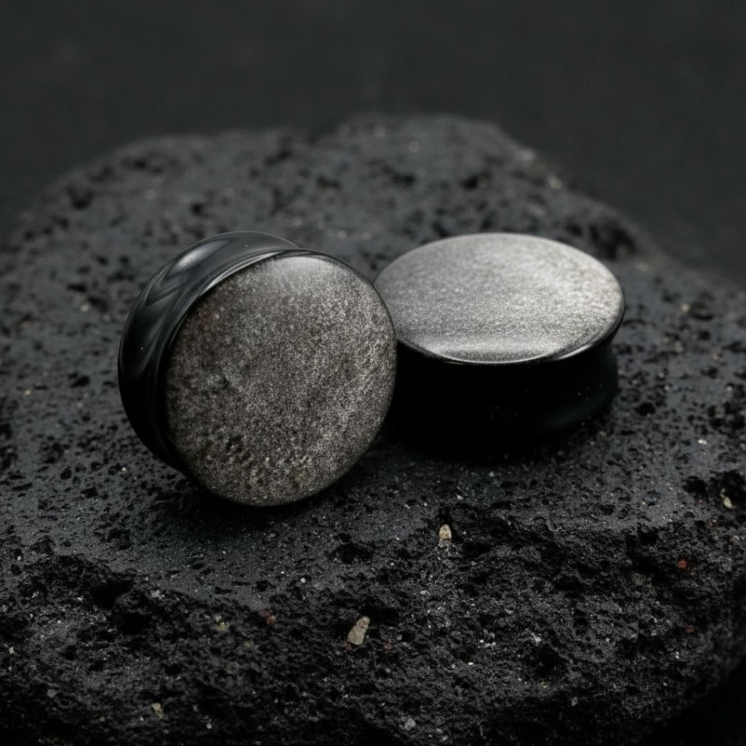 Pair of deep black Silver Obsidian stone plugs, polished, reflecting a subtle silver flash. Gauges displayed on a dark background.