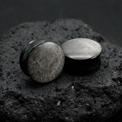 Pair of deep black Silver Obsidian stone plugs, polished, reflecting a subtle silver flash. Gauges displayed on a dark background.