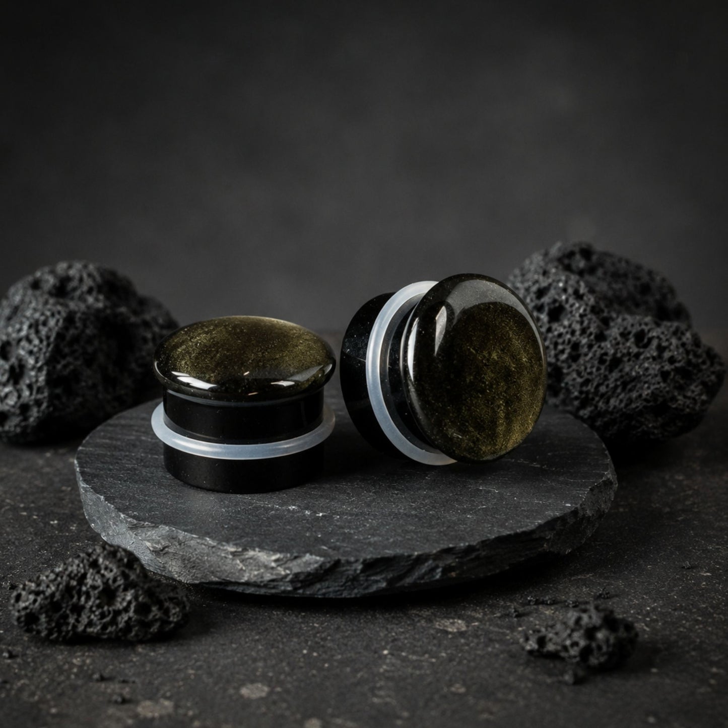 Single Flare Golden Obsidian stone plugs on top of smooth black volcanic stone