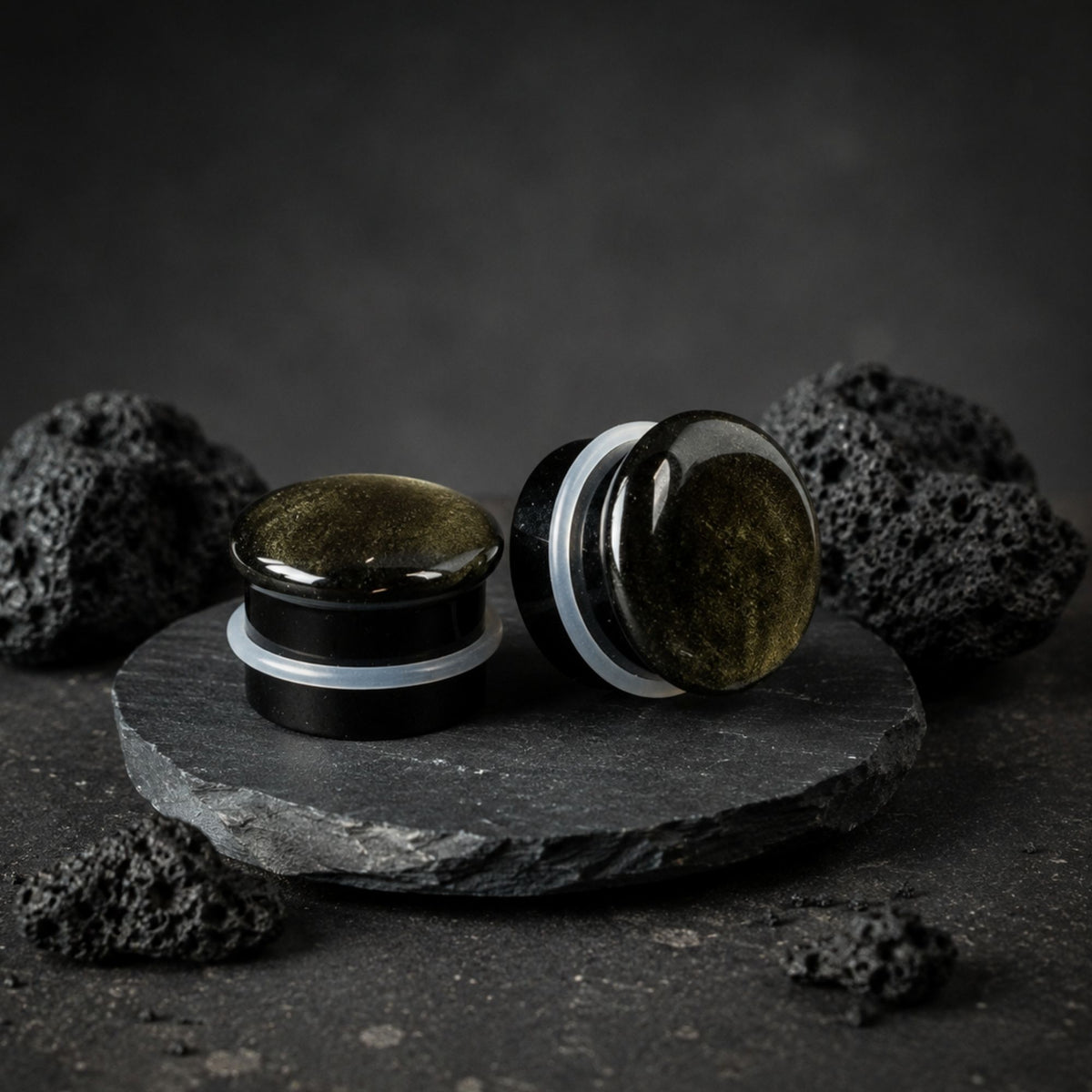Single Flare Golden Obsidian stone plugs on top of smooth black volcanic stone