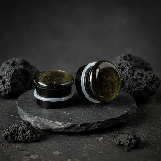 Single Flare Golden Obsidian stone plugs on top of smooth black volcanic stone