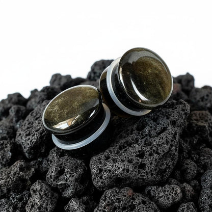 Single flare golden obsidian stone plugs shown up close. Dark gauges with gold flashes, suitable for stretched ear piercings