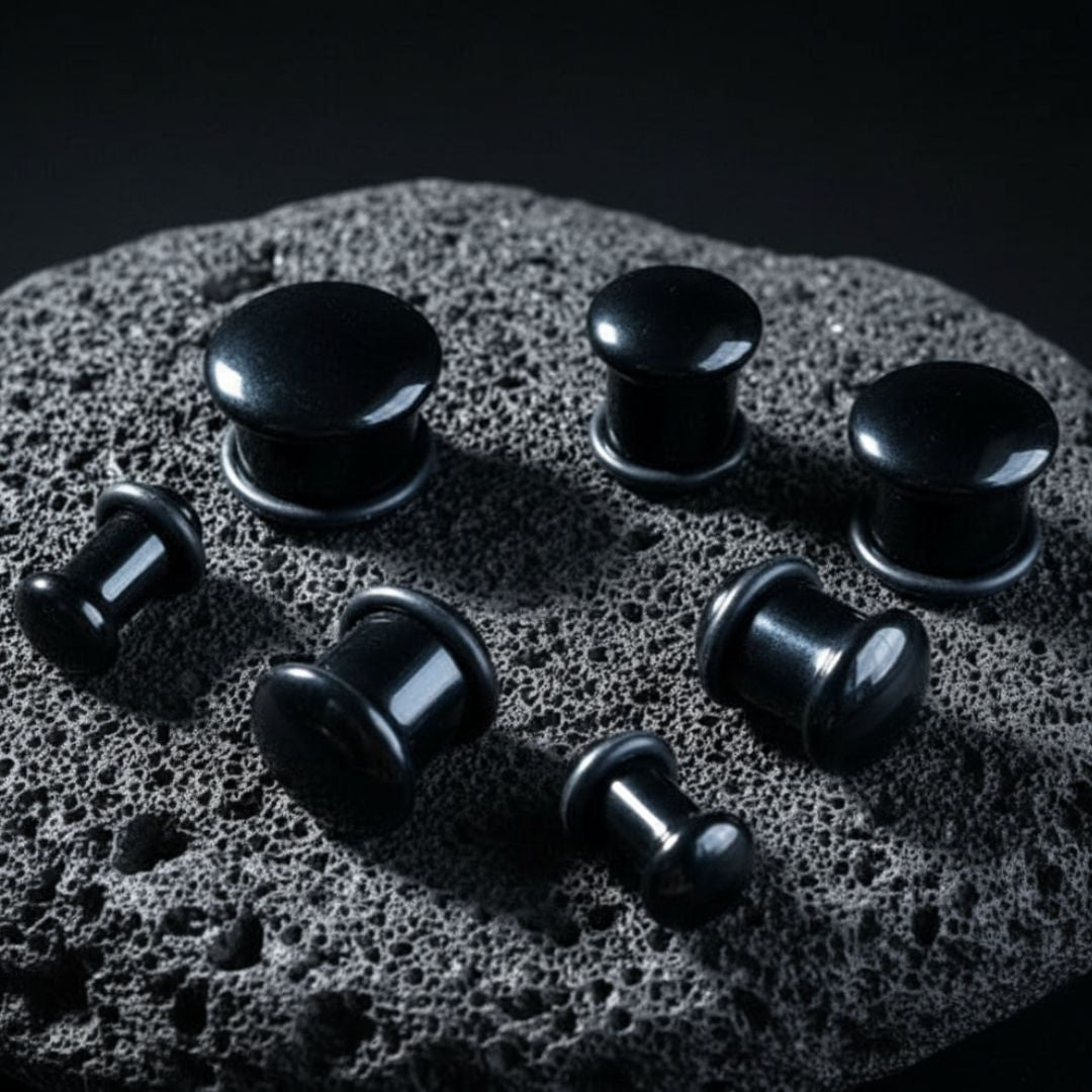 A pair of Single Flare Onyx Stone Plugs on dark volcanic rock with dramatic lighting.
