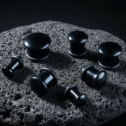 A pair of Single Flare Onyx Stone Plugs on dark volcanic rock with dramatic lighting.