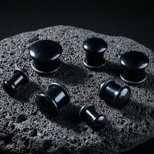 A pair of Single Flare Onyx Stone Plugs on dark volcanic rock with dramatic lighting.