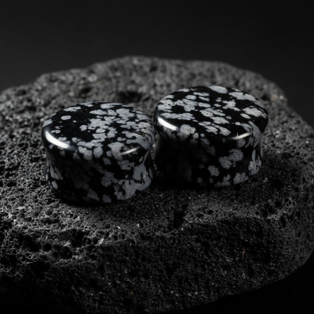 Pair of Snowflake Obsidian plugs resting on a dark surface. Black and white natural stone gauges for stretched lobes.