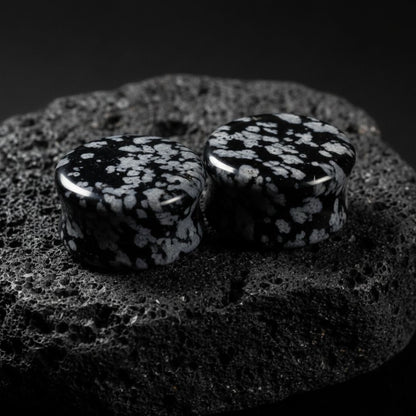 Pair of Snowflake Obsidian plugs resting on a dark surface. Black and white natural stone gauges for stretched lobes.