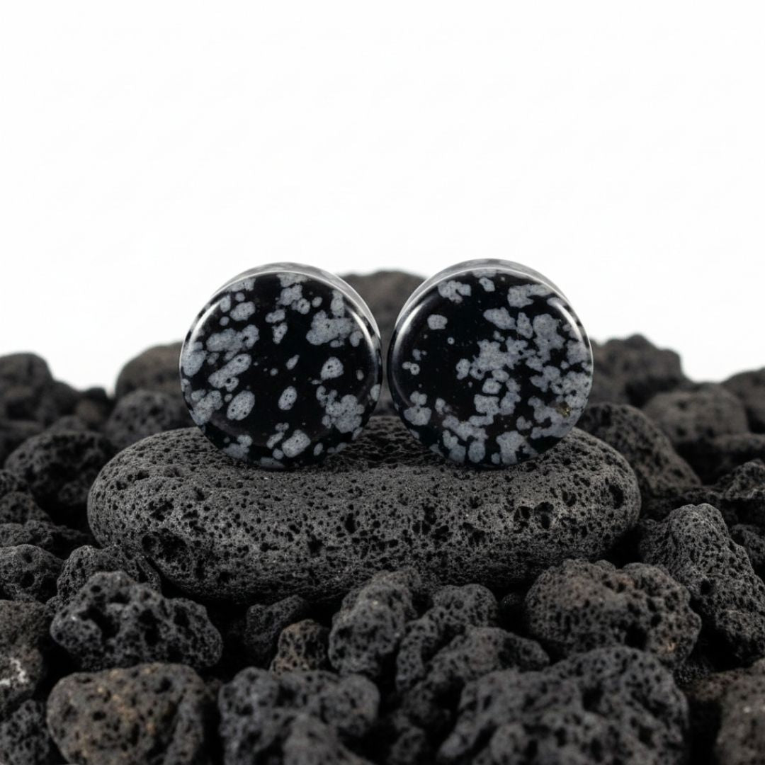 Pair of Snowflake Obsidian plugs resting on a dark surface. Black and white natural stone gauges for stretched lobes.