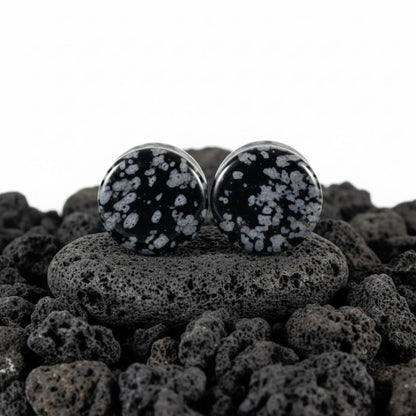 Pair of Snowflake Obsidian plugs resting on a dark surface. Black and white natural stone gauges for stretched lobes.