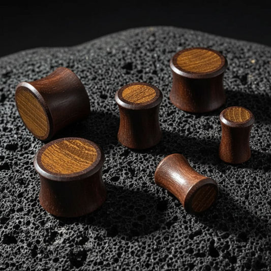 Sono Wood Plugs with Teak inlay on volcanic stone with dark, cinematic lighting.