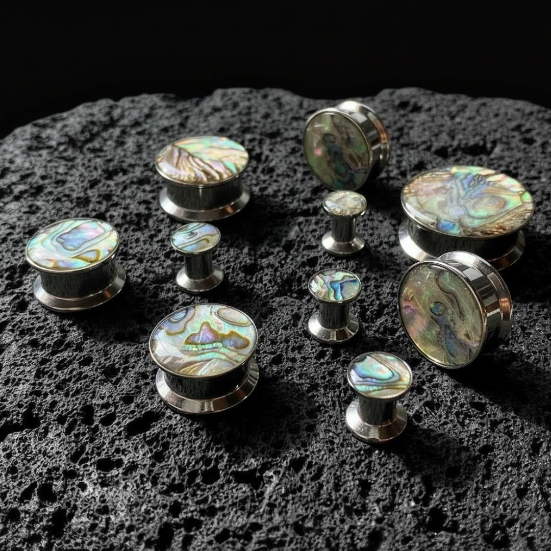 Steel Abalone Inlay Plugs (6mm-25mm) on dark volcanic rock with dramatic lighting.