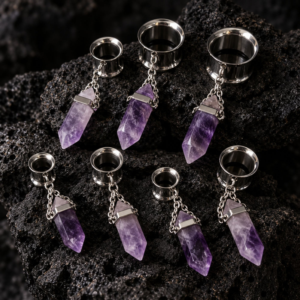 Steel Amethyst Dangle Tunnels (6mm-16mm) on dark volcanic rock with sharp shadows.