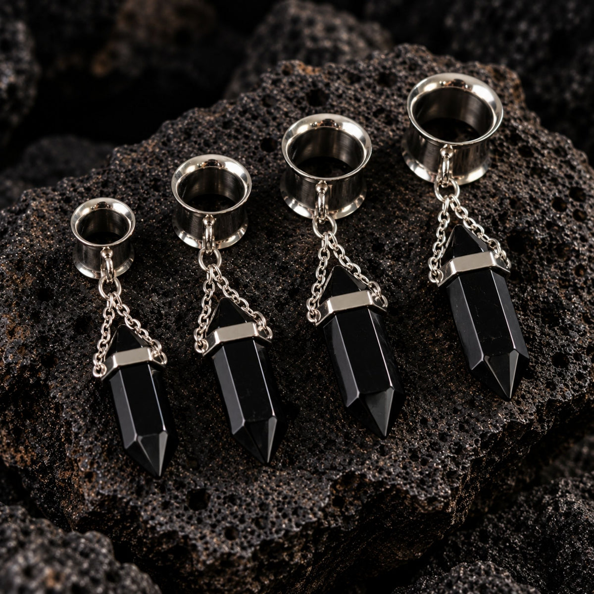 A pair of Steel Onyx Dangle Tunnels on dark volcanic rock with dramatic side lighting.