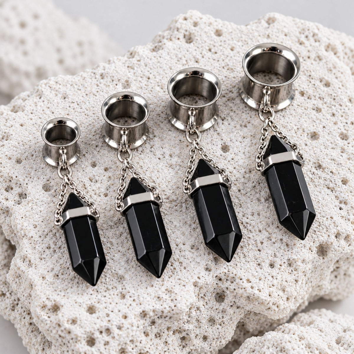 Close-up of the Steel Onyx Dangle Tunnels on volcanic stone against a clean white background.