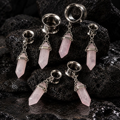 Steel Rose Quartz Dangle Tunnels on dark volcanic stone with dramatic side lighting.
