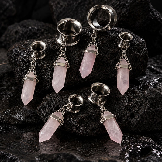 Steel Rose Quartz Dangle Tunnels on dark volcanic stone with dramatic side lighting.